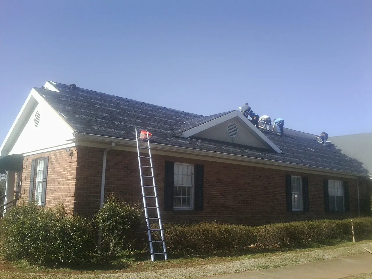 Crew tearing shingles off a brick ranch roof with a ladder set — Metal Roof Repair work by our crew in Alexandria